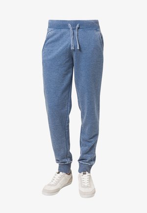 Un pantalon de survêtement en tissu bleu doux, avec une taille à cordon de serrage, des chevilles côtelées et des poches latérales. Associé à des baskets blanches.