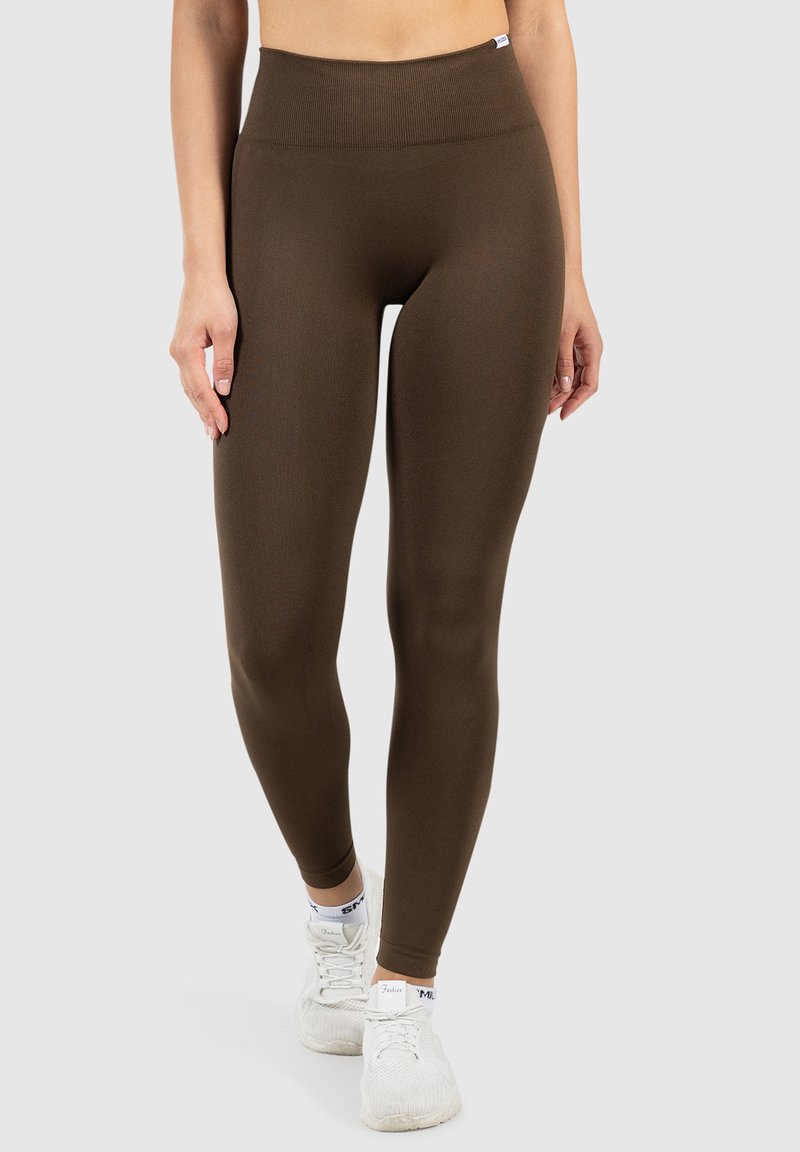 Bruine high-waisted leggings met een gladde, elastische textuur. Gemaakt in combinatie met witte sportschoenen, wat een strakke, gestroomlijnde vorm toont.