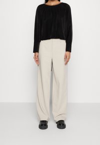 Blouse noire à manches longues avec un col froncé, associée à un pantalon crème à jambes larges et des chaussures compensées noires. Tissu lisse et coupe décontractée.