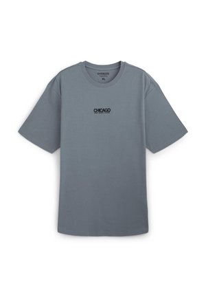 T-shirt grigia oversize in cotone, con maniche corte e scollo rotondo. Testo nero "CHICAGO RAW MUSIC SCENE" sulla parte anteriore.