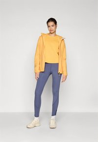 Geltonas gobtuvu aprengtas švarkas virš geltono viršutinio drabužio, derinamas su mėlynomis tamprėmis. Aprang�ą užbaigia balti sportbačiai. Lygus audinys, laisvas kirpimas.