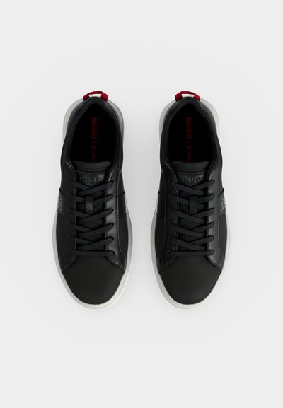 Paire de baskets basses noires avec semelles blanches, lacets noirs, languettes rouges au talon et marquage "HUGO" à l'intérieur et sur la languette.