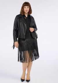 Czarna skórzana kurtka motocyklowa z srebrnymi zamkami błyskawicznymi, w połączeniu z czarną spódnicą z frędzlami. Obie części charakteryzują się gładkimi teksturami i dopasowanym krojem.
