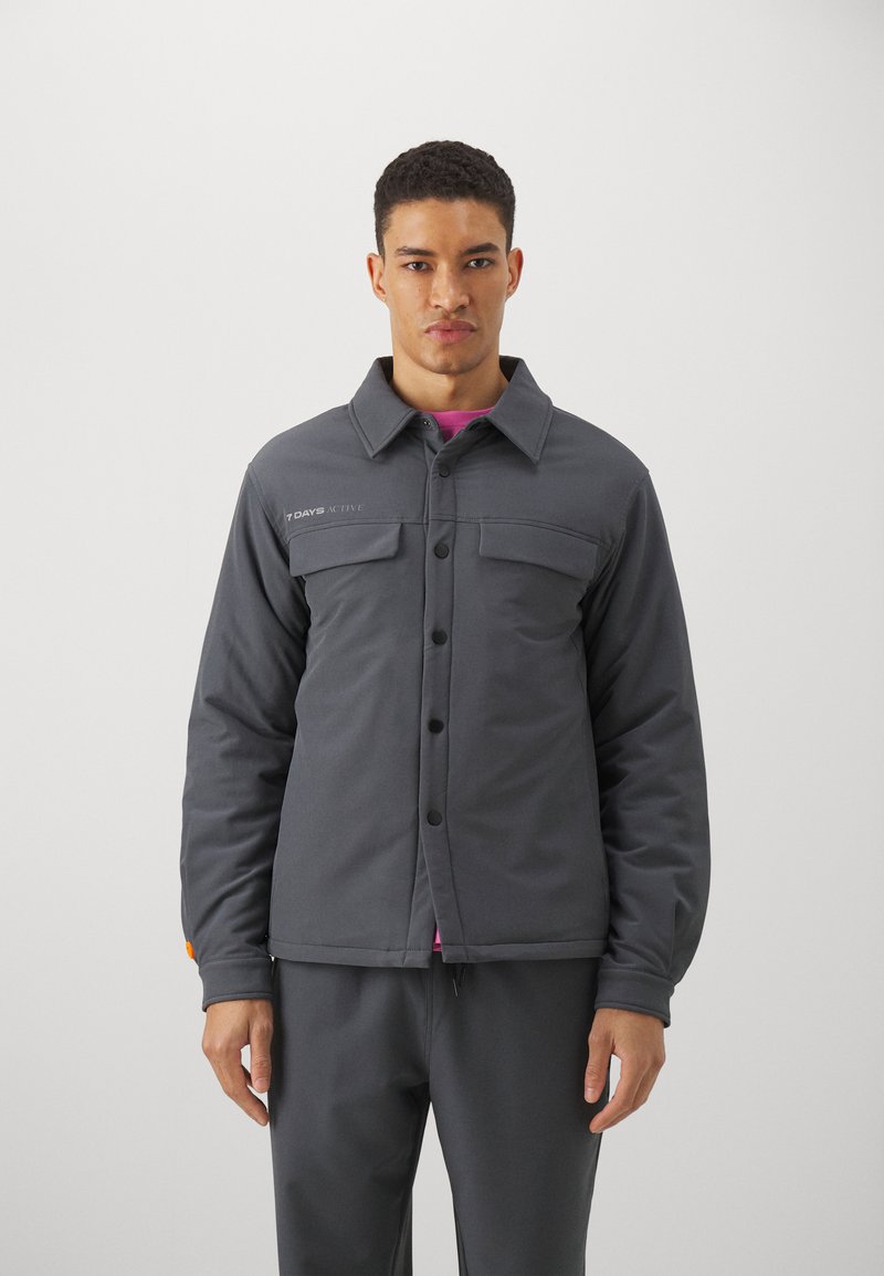 Gray insulated jacket with a collar, front snap closure, two chest pockets, and a logo. Smooth texture with a fitted design.