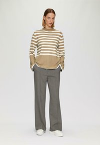 Beige und weiß gestreifter Strickpullover mit langen Ärmeln, kombiniert mit grauen, maßgeschneiderten Hosen und weißen Sneakers. Einfaches Design, lässige Passform.