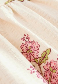 Blødt cremefarvet stof med teksturerede striber og mønster af pink blomster og broderi af grønne blade.