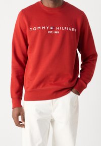 Czerwona bluza z okrągłym dekoltem, z logo "TOMMY HILFIGER EST. 1985" w białym i niebieskim kolorze. Wykonana z miękkiej bawełny, z ściągaczami przy rękawach i na dole.