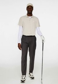 Beige pikétröja med krage, grå byxor, vit långärmad undertröja, vit handske, svartvita sneakers och en beige keps. Golfklubba i handen.