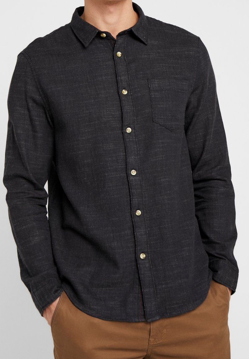 Granatowa koszula na guziki o tkanej fakturze, z kieszenią na piersi, długimi rękawami i kontrastowymi jasnymi guzikami.
