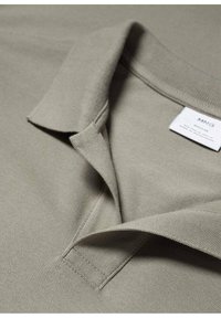 Polo beige avec un tissu texturé, doté d'un col plié et de coutures détaillées. Étiquette de la marque visible près de l'encolure.