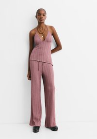 Žebrovaný, světle růžový halter top spojený s volnými širokými kalhotami ve stejné barvě. Materiál je texturovaný, což zvýrazňuje volný střih.