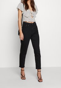 Biała bluzka w czarne kropki, z falbaniastymi rękawami i głębokim dekoltem, zestawiona z czarnymi spodniami o wysokim stanie i czarnymi sandałkami na obcasie.