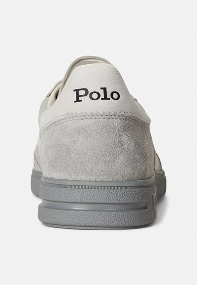 Grå mockasinsneaker med en vit läderklack som har svart texten "Polo". Den strukturerade gummisulan ger bra grepp.