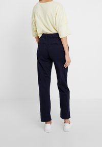 Lös passform gul T-shirt med korta ärmar, kombinerad med marinblå byxor med resårlinning och bakfickor.