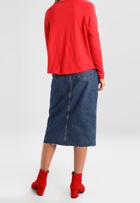 Punainen pitkähihaista paita, farkku midi-hame, jossa on raaka helma, ja punaiset nilkkurit. Asuste yhdistää tekstuureja ja värejä rentoon tyyliin.