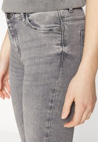 Jeans de mezclilla en gris con un corte ajustado, desvanecimiento sutil y diseño de cinco bolsillos. El hardware metálico en la parte frontal añade un detalle estructural.