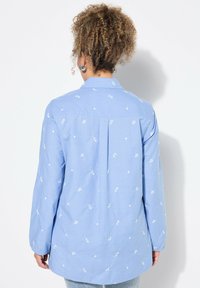 Camicia button-up azzurro chiaro con ricami floreali bianchi, maniche lunghe, colletto e dettaglio a piega sul retro. Materiale in misto cotone.