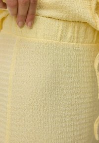 Tissu jaune texturé avec un design extensible et froissé. La taille est élastique, et il y a des coutures visibles le long des bords.
