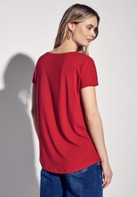 Top rosso a maniche corte con scollatura rotonda, trama morbida, vestibilità comoda e orlo arrotondato, abbinato a jeans in denim blu.