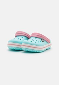 Light blue clogs with a pink strap, featuring ventilation holes and a white and pink striped sole. Made from flexible material.