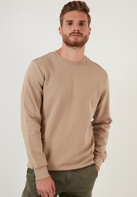 Sudadera de manga larga color beige claro con textura acanalada, cuello redondo y puños ajustados, combinada con pantalones cargo color verde oliva.