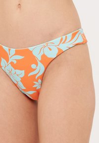 Orange bikiniunderdelar med ett blommönster i ljusblått. Tillverkade av smidigt material med låg midja och minimal täckning.