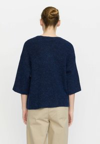 Mørkeblå strikket sweater med en afslappet pasform, brede ærmer og strukturdetail, parret med beige bukser.