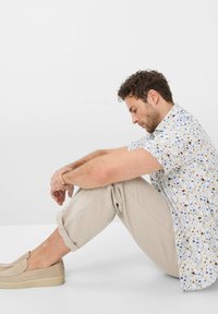 Short-sleeve shirt with a floral print in white, blue, and brown, paired with rolled beige linen pants and light beige slip-on shoes.
