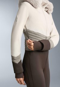 Könnyű steppelt dzseki krém és szürke színben, műszőrme gallérral, cipzáras záródással és bordázott mandzsettákkal. Testhez simuló szabás vonzó kialakítással.