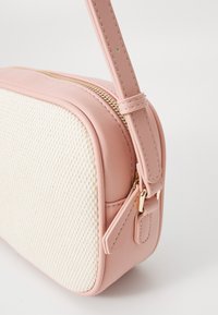 Συμπαγής τσάντα με ροζ δερμάτινη κορυφή και κρεμ υφασμάτινες πλευρές, διαθέτει χρυσό φερμουάρ και ρυθμιζόμενο ιμάντα.