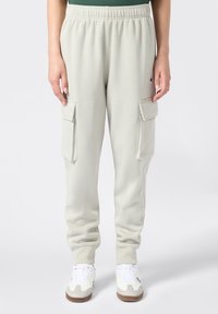 Hellgraue Sweatpants mit elastischem Bund und Cargo-Taschen auf beiden Seiten. Hergestellt aus weichem Stoff und kombiniert mit weißen Turnschuhen.