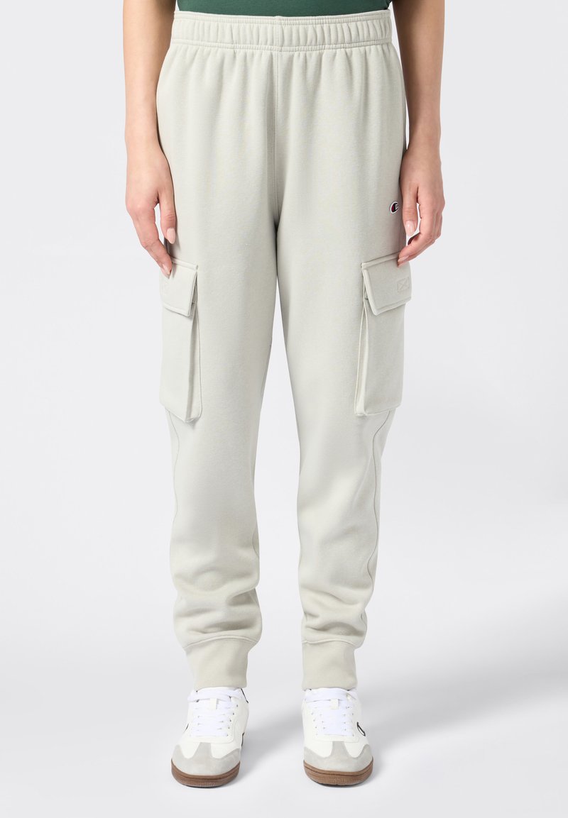 Hellgraue Sweatpants mit elastischem Bund und Cargo-Taschen auf beiden Seiten. Hergestellt aus weichem Stoff und kombiniert mit weißen Turnschuhen.