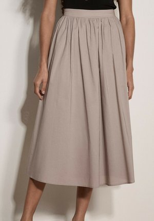Beżowa spódnica midi z wysokim stanem i plisami, noszona przez osobę stojącą na jednolitym jasnym tle.