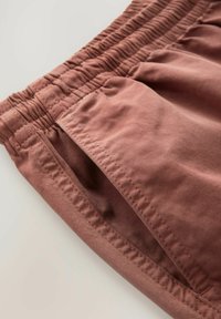Zachte stof in een stofkleurige rozenkleurige short met een elastische tailleband, zijzakken en subtiele stiksels.