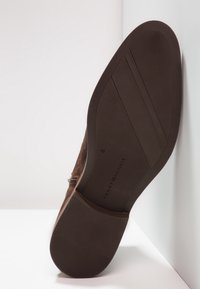 Soletta di scarpa in suede marrone con design della trazione in gomma; include logo del marchio e stampa delle taglie. Tacco piatto e superficie liscia.