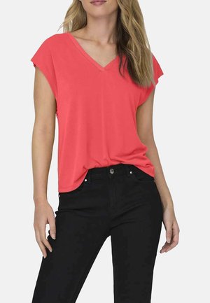 T-shirt corail à col en V avec manches courtes, confectionné en tissu doux, associé à un jean noir, mettant en avant un design et une coupe décontractés.