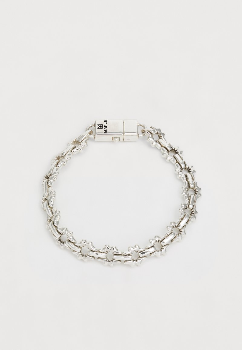 Sudraba aproce ar sarežģītu dizainu, kura rotājumā ir zvaigžņu formas akcenti un uzticams aizdare. Virsma ir gluda un ar pulētu apdari.