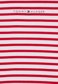 Rød og hvidt stribet bomuldsstof med et logo, der siger "TOMMY HILFIGER" og "EST. 1985" i blå broderi.