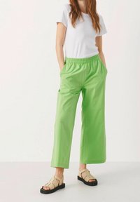 Pantalon large vert avec une taille élastique et des poches, associé à un t-shirt blanc et des sandales beiges. Tissu lisse, design décontracté.