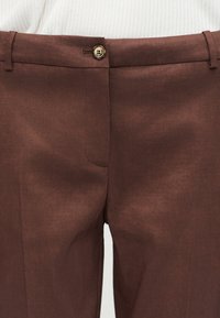 Καφέ ραμμένο παντελόνι με κούμπωμα κουμπιού και φερμουάρ, θηλιές για ζώνη και λευκό ριμπ μπλουζάκι φορεμένο μέσα στη μέση.