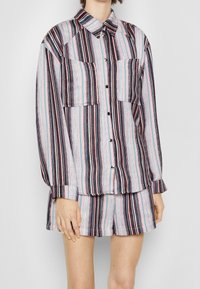 Chemise à boutons rayée multicolore, dotée de deux poches avant, de longues manches et d'un col, associée à un short assorti.