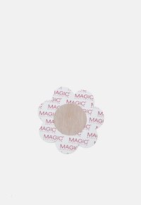 Patch adhésif en forme de fleur avec une zone centrale beige, entourée de papier blanc portant le texte rouge "MAGIC BODYFASHION". Texture lisse.