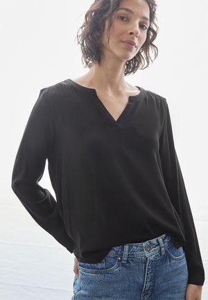 Schwarze Bluse mit langen Ärmeln und V-Ausschnitt, weicher Textur und gerafften Schultern, kombiniert mit blauen Jeans.