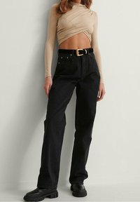 Jeans neri a vita alta con una vestibilità comoda, abbinati a una maglietta beige a maniche lunghe con un design attorcigliato. Scarpe nere con suola spessa.