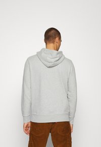 Grijze katoenen hoodie met een aantrekkoord in de capuchon, ribbelmanchetten en een ribbelzoom. Gekozen in combinatie met een bruine corduroy broek. Achteraanzicht.