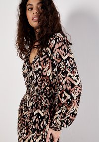 Langärmliges Kleid mit einem abstrakten Muster in Schwarz, Braun und Creme, tiefem V-Ausschnitt und elastischem Taillenbund für eine figurbetonte Silhouette.