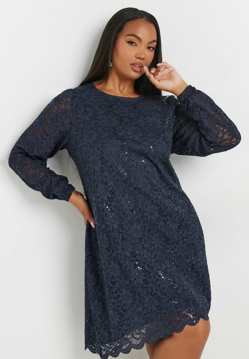 Vestido de encaje azul marino con mangas largas, patrones florales, dobladillo en forma de pico y sutiles lentejuelas. Textura suave, ajuste relajado, escote redondo.