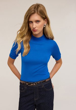 Blauwe nauwsluitende trui met korte mouwen en hoge kraag, gemaakt van glad gebreide stof. Heeft ribbelaccenten bij de halslijn en mouwen.