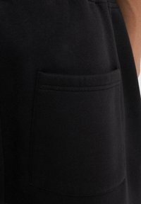 Svarte bomullsshorts med et enkelt design, synlig sidelomme og glatt tekstur.