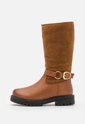 Botte mi-mollet en cuir et daim marron avec une semelle noire épaisse et un détail de sangle à boucle dorée sur le côté.